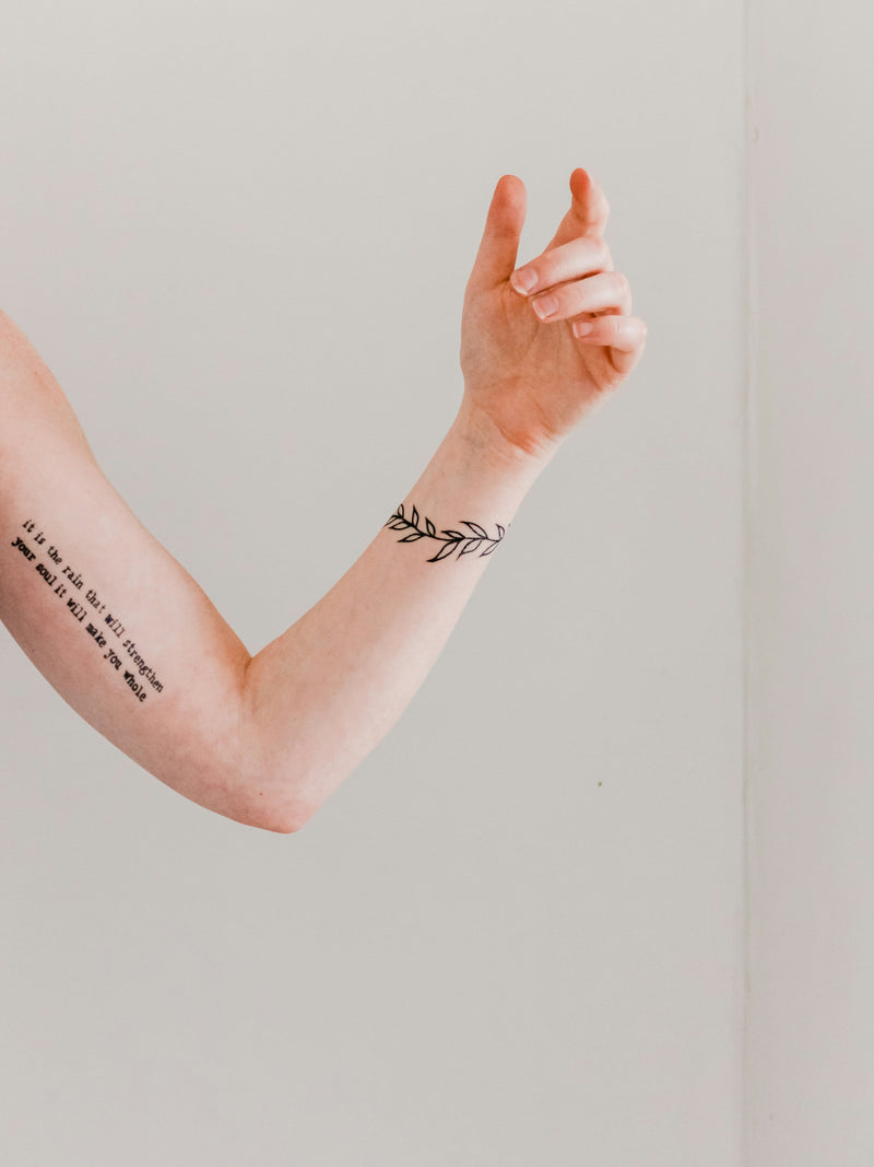 A forearm with fine-line tattoos against a plain wall in soft light.