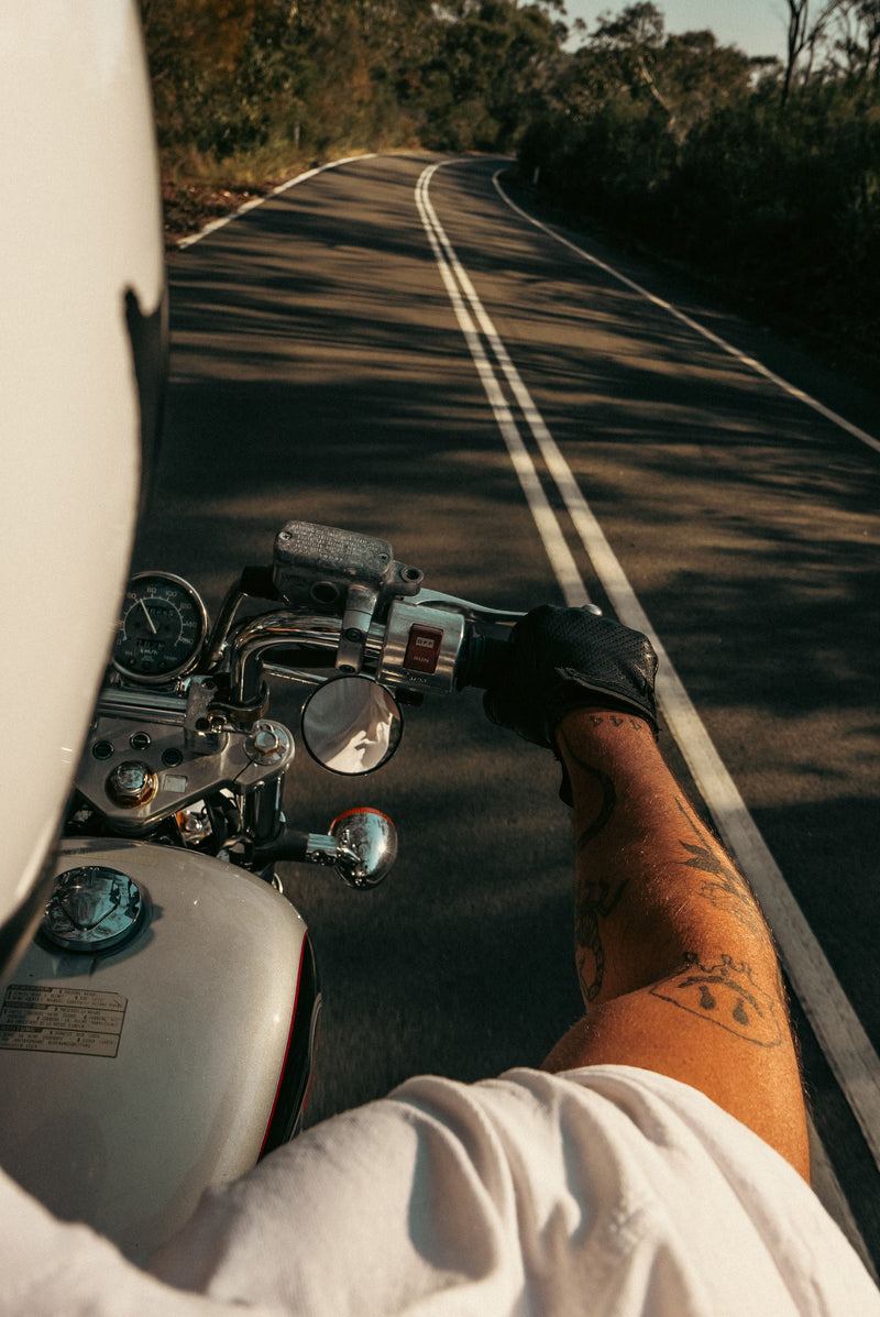 A tattooed forearm on a motorcycle throttle, open road ahead. A reminder that ink does not have to be permanent.