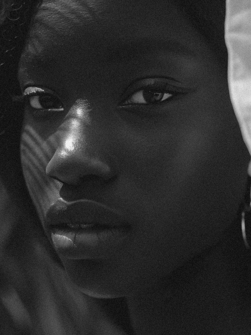 Editorial side-profile portrait of a woman with deep skin tone and healthy, even skin in soft light.