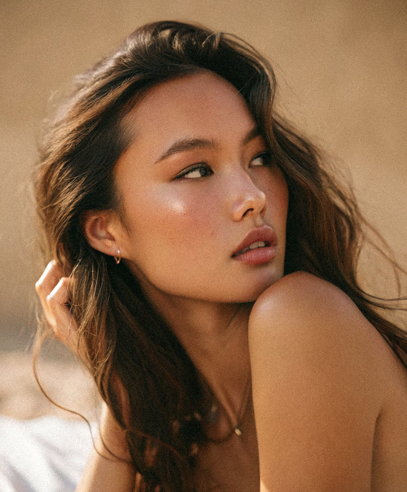 Editorial portrait of a young woman with long wavy hair and gold drop earrings, in warm golden light.