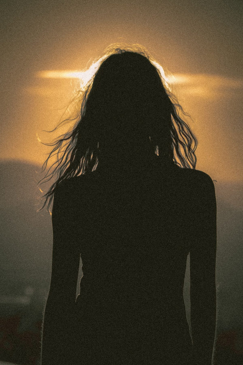 Golden-hour editorial silhouette of a woman with long hair, backlit by warm light.