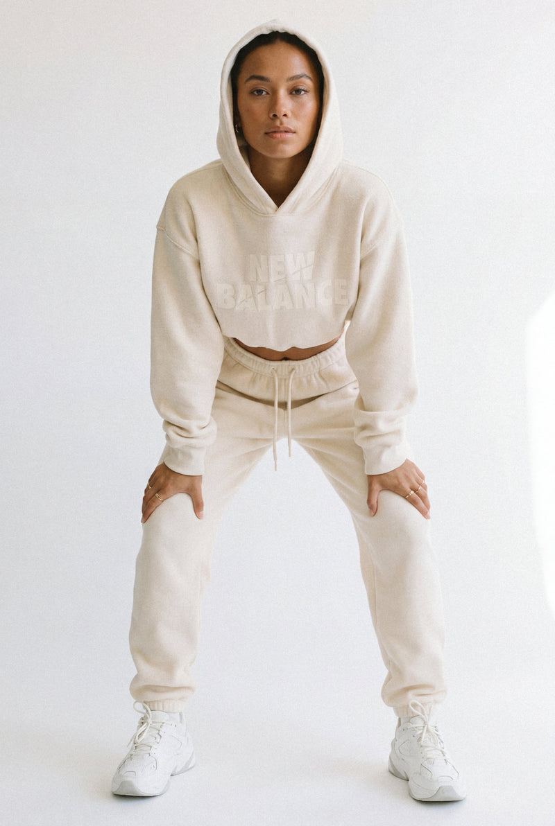 Woman in a cream hoodie and joggers in an athletic half-squat, focused on muscle tone.