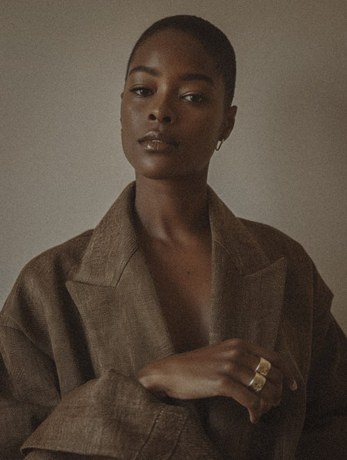 Portrait of a woman with deep skin tone in a brown linen shirt against a neutral background