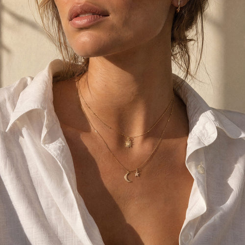 Woman wearing layered necklaces in natural sunlight, face turned to the light