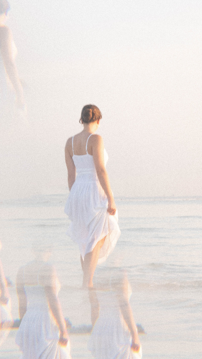 Woman in a white dress walking into a calm sea in soft morning light