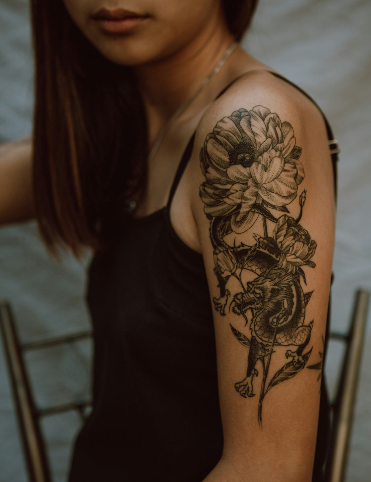 A detailed floral and dragon tattoo on a woman's upper arm. Deeper skin tones treated to the same standard.