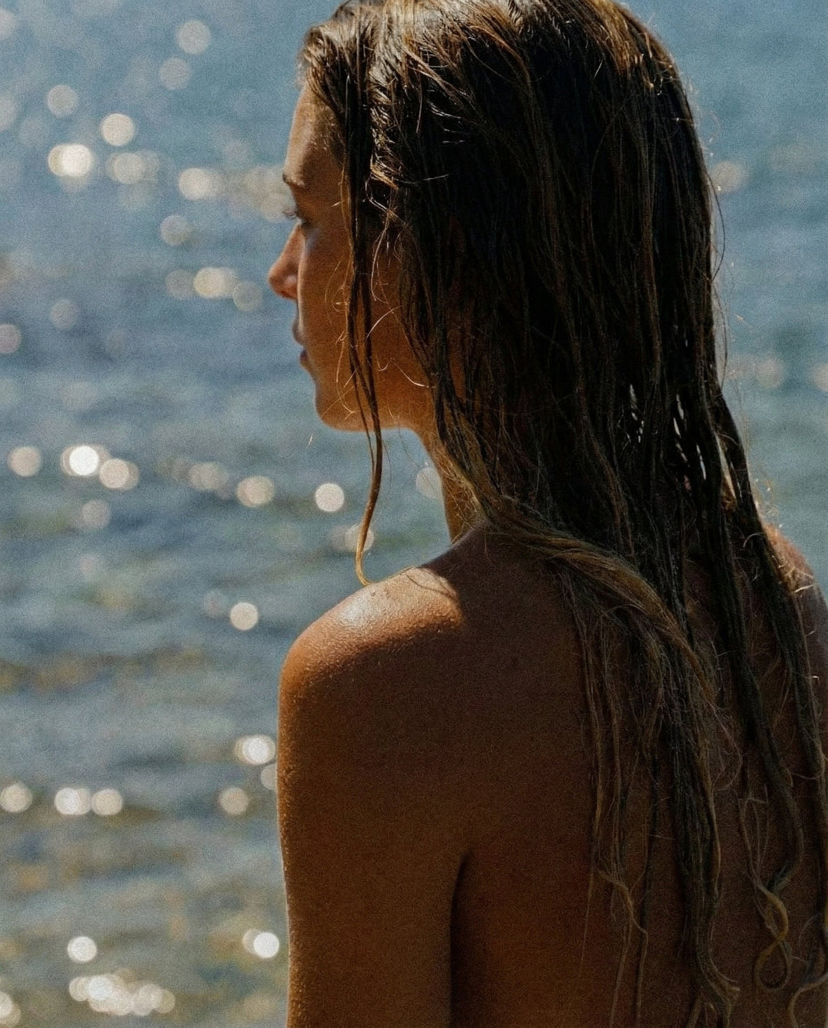 Woman by sparkling water, bare shoulders in sunlight
