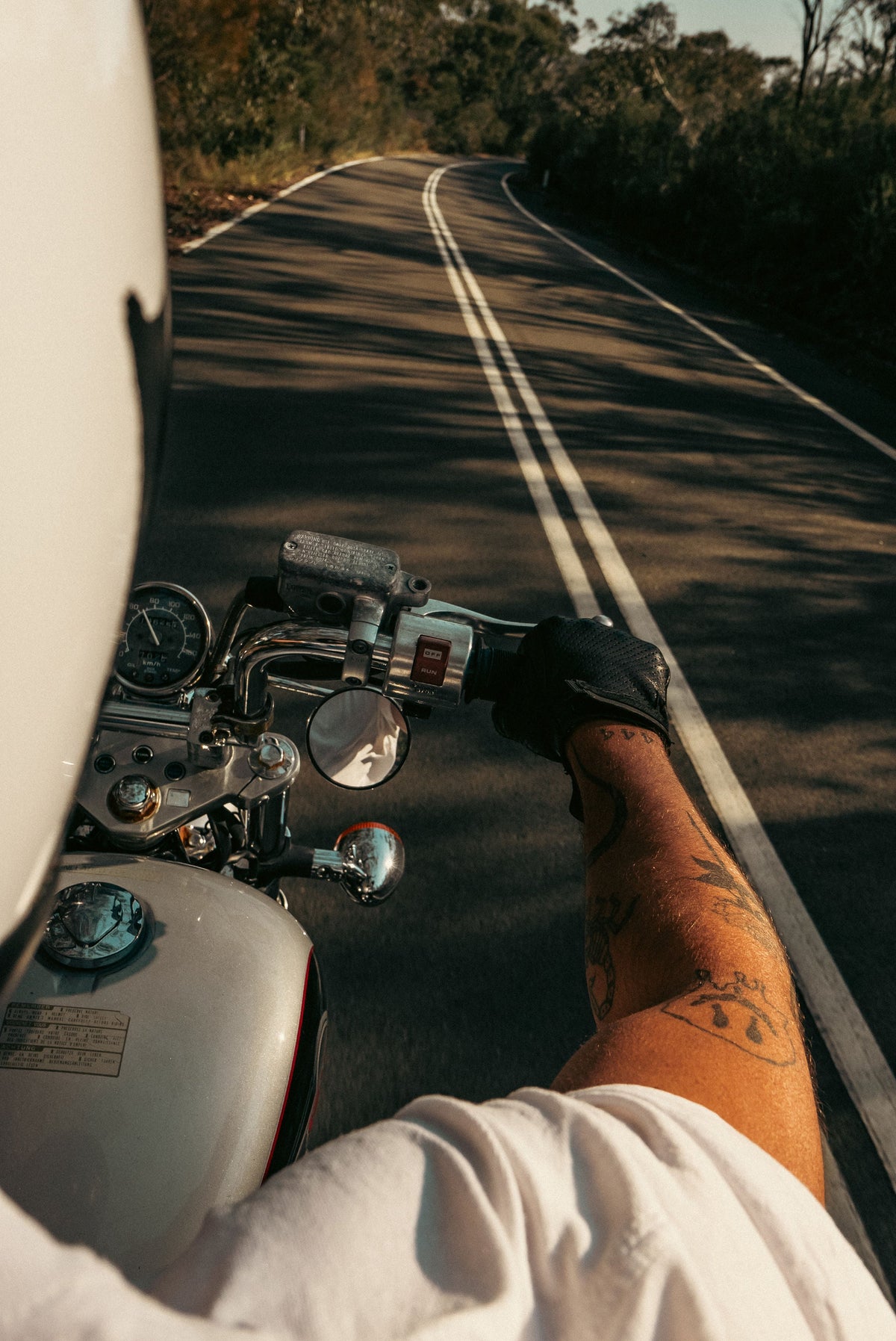 A tattooed forearm on a motorcycle throttle, open road ahead. A reminder that ink does not have to be permanent.