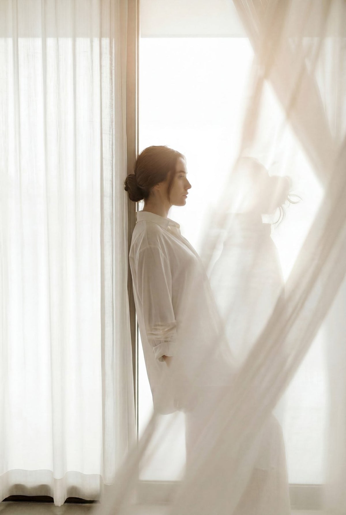 Editorial portrait of a woman by a sunlit window, calm and serene.