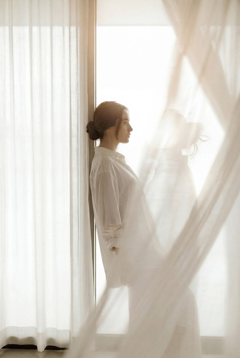 Editorial portrait of a woman by a sunlit window, calm and serene.