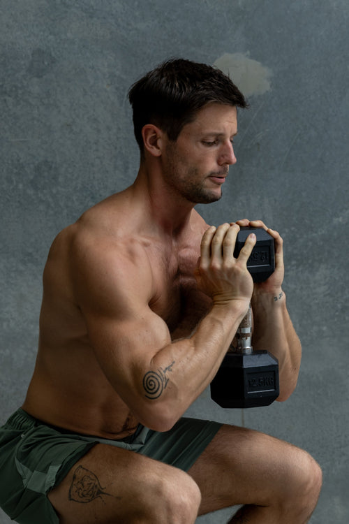 Fit, shirtless man crouching while holding a kettlebell during strength training.