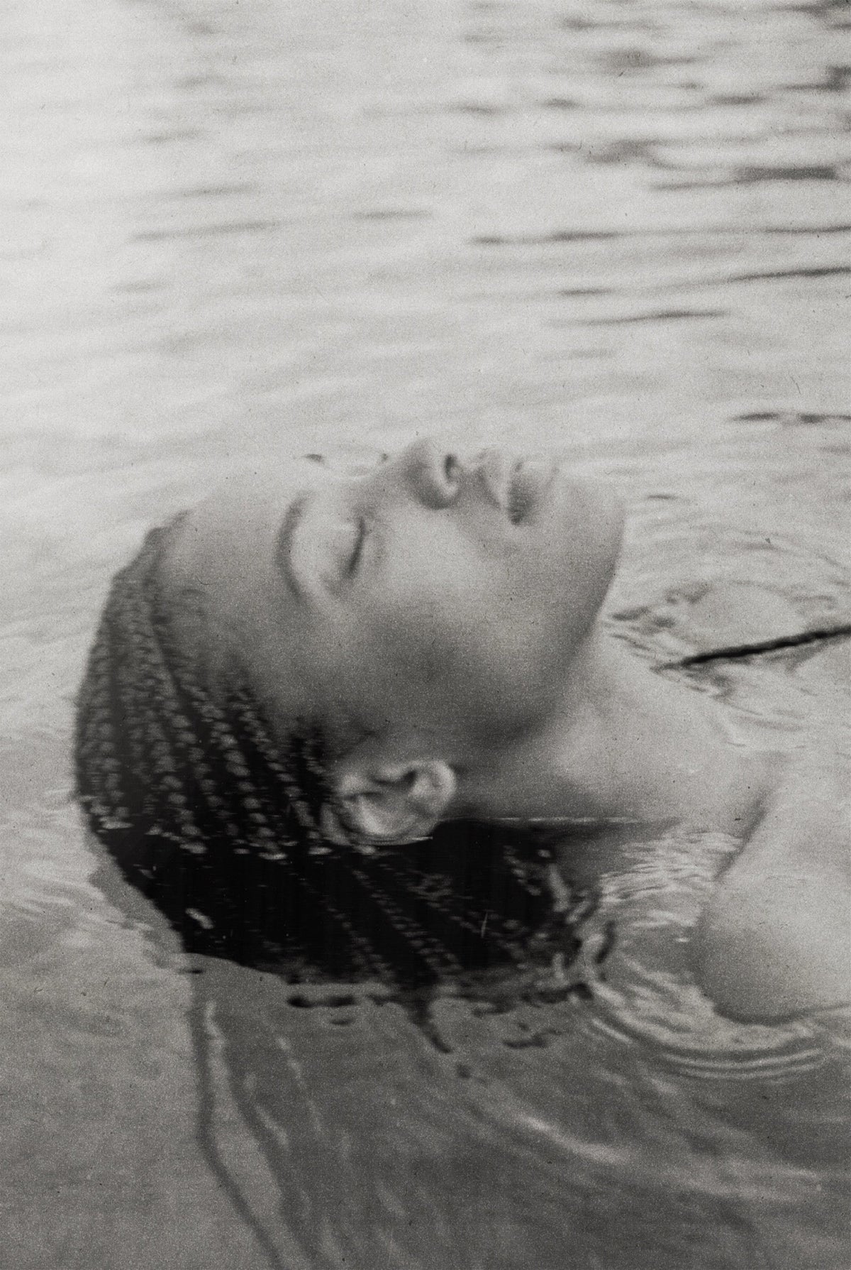 A woman's face resting in water, eyes closed, serene, in black and white.