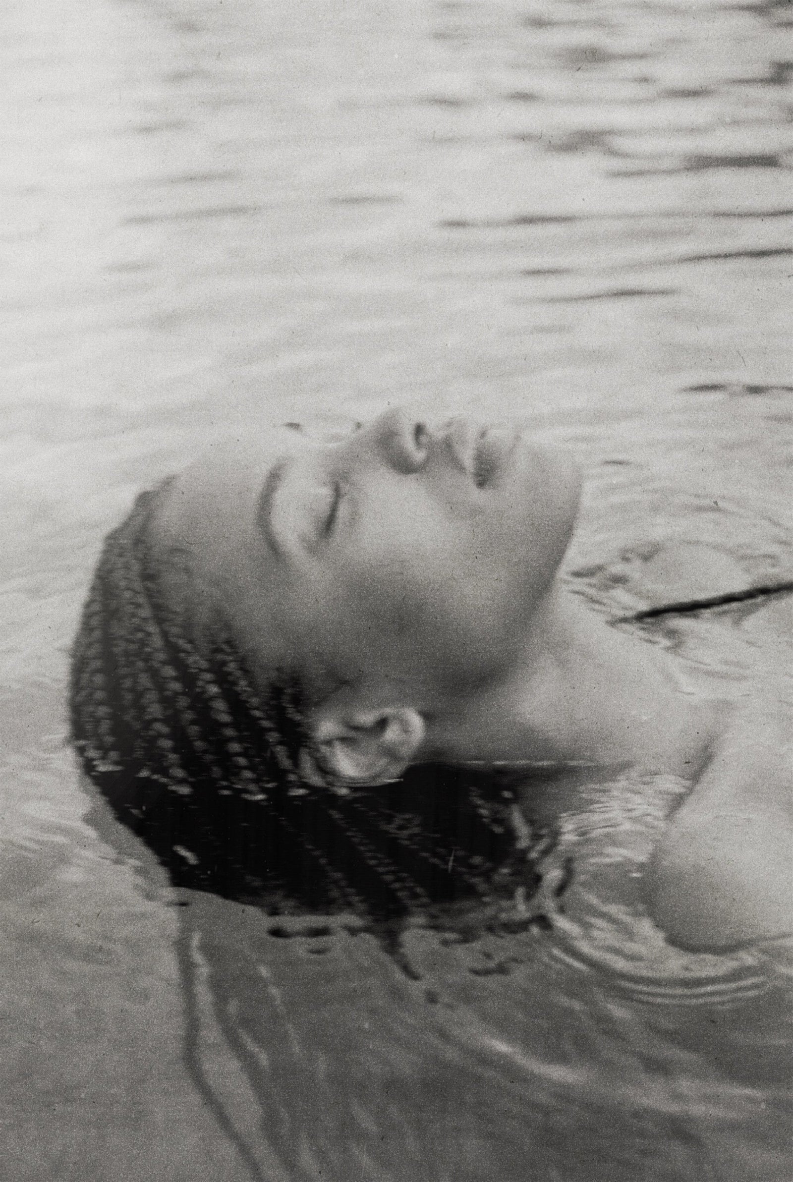 A woman's face resting in water, eyes closed, serene, in black and white.