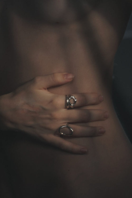 Editorial close-up of a hand with fine silver rings resting on bare skin.