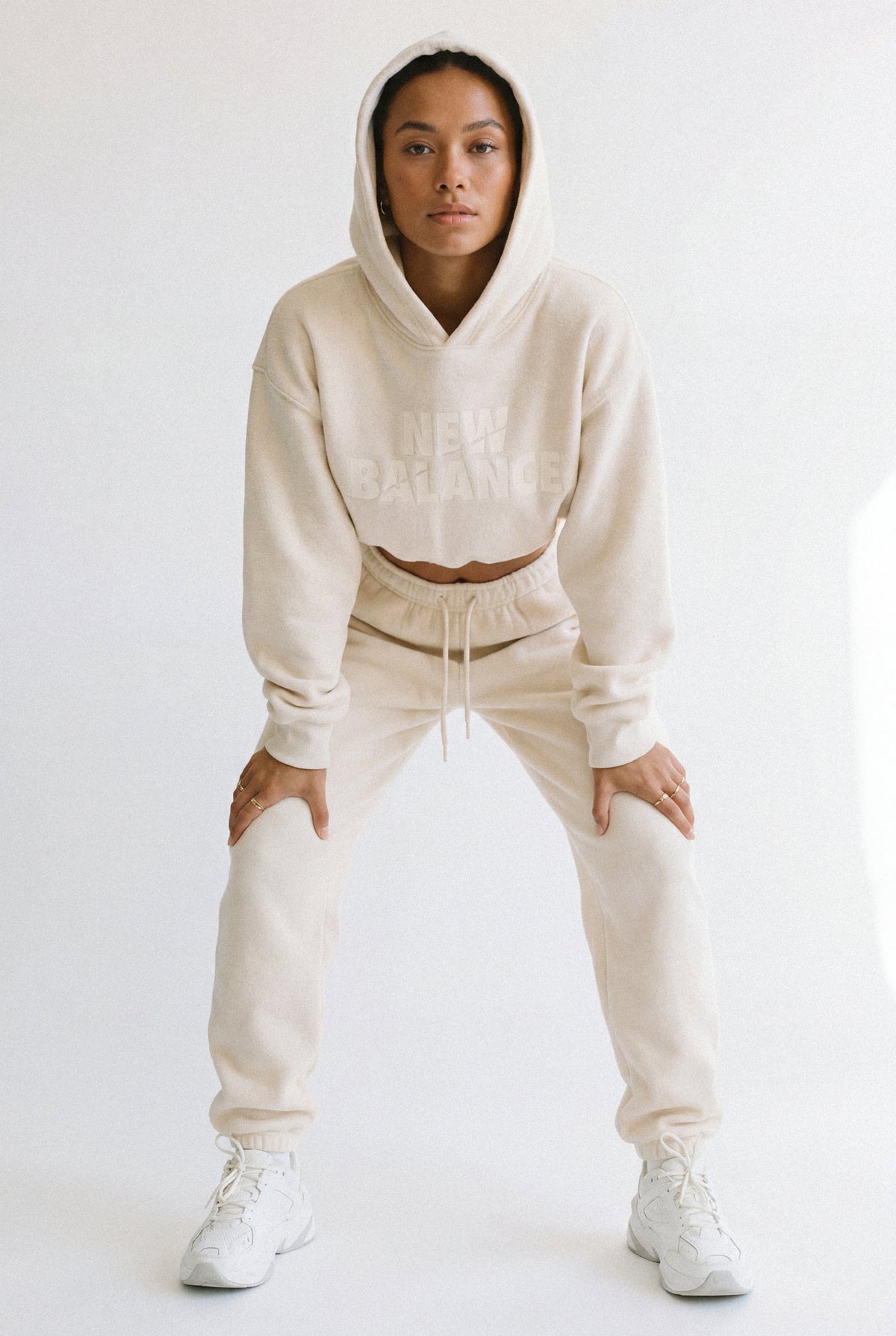Woman in a cream hoodie and joggers in an athletic half-squat, focused on muscle tone.