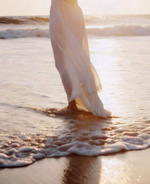 Bare legs wading through shallow water at sunset