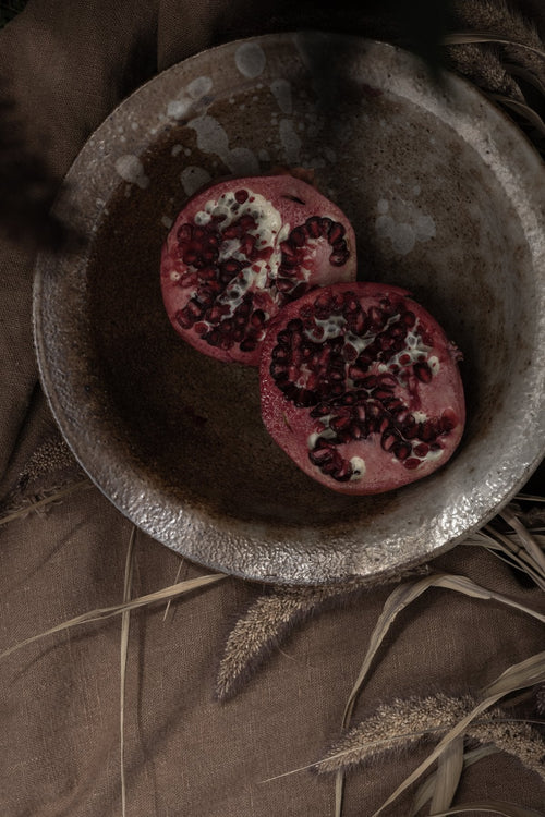 Halved pomegranate with bright red seeds in a rustic bowl