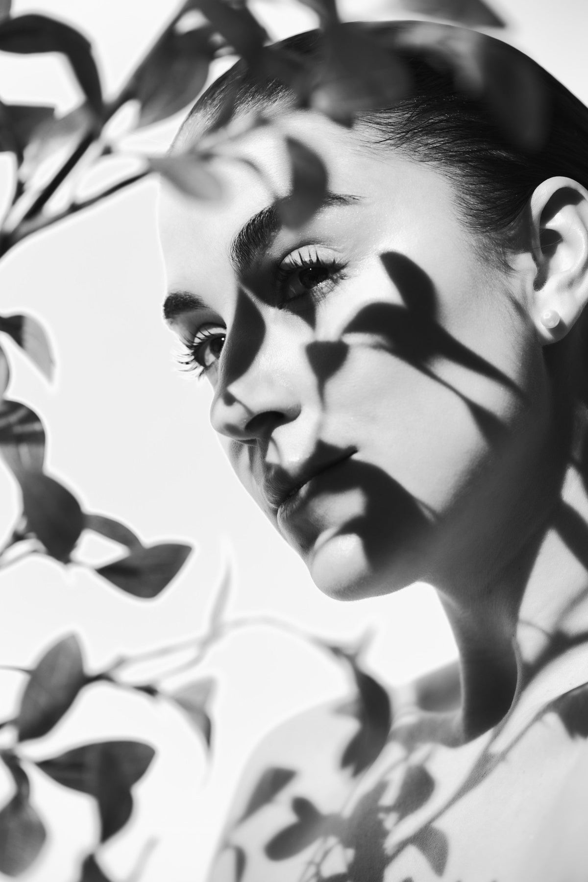 Black-and-white portrait of a woman with dappled light across calm, even skin.
